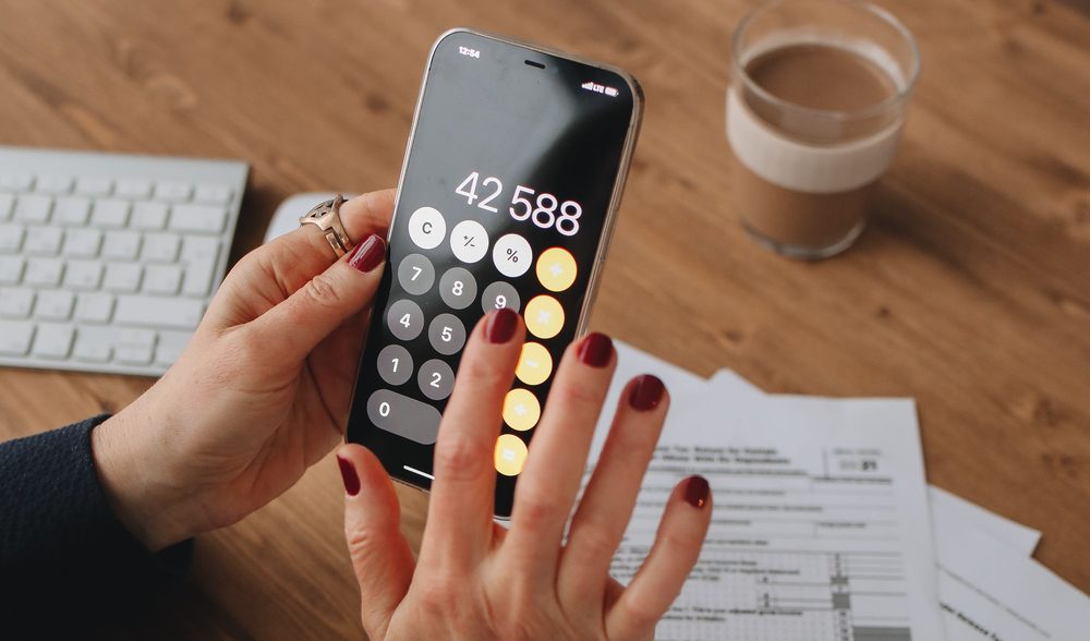 Manos con un celular usando la calculadora sobre un escritorio con formularios impositivos